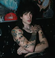 a man with lots of tattoos on his arm and chest sitting in front of balloons