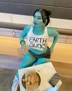 a woman with blue paint on her body sitting next to a box of doughnuts