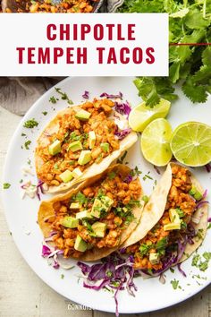 two tacos on a plate with limes and cilantro