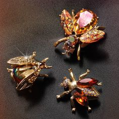 three bee brooches sitting next to each other on a black surface with red and yellow crystals