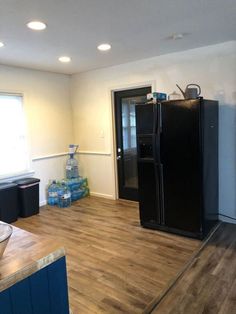 a kitchen with wood floors and black refrigerator freezer next to window on the wall