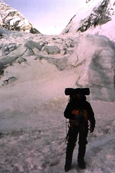 a man standing in the snow with skis on his head and backpack over his shoulder