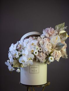 a white bucket filled with lots of flowers on top of a metal stand in front of a gray wall