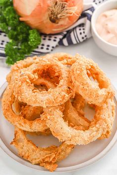 onion rings on a white plate next to some dipping sauces and an onion plant