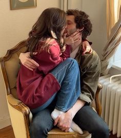 a man and woman sitting on top of a chair kissing in front of a radiator