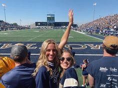 two women and a man at a football game waving to the crowd with their arms in the air