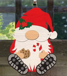 a wooden sign with a santa clause holding a candy cane and cookies on it's chest