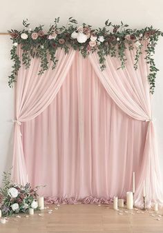 a pink backdrop with roses and greenery on the top is decorated with candles for a wedding ceremony