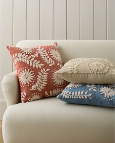 three pillows stacked on top of each other in front of a white couch with wood paneling