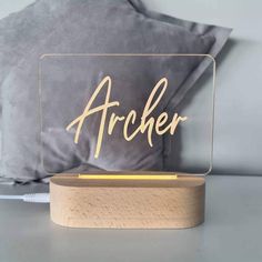 an acrylic sign with the word archer on it sitting next to a pillow