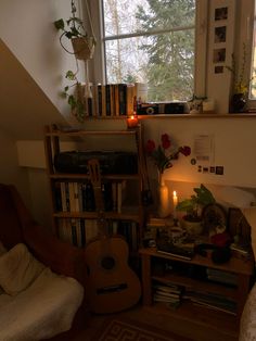 a room with a guitar, bookshelf and candles on the floor in front of a window