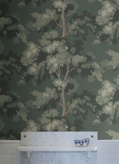 a white toilet sitting in a bathroom next to a wallpaper covered in green trees