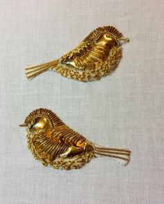 two gold bird brooches with chains on them