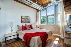 a bedroom with wood floors and white walls has a red blanket on the bed in front of large windows