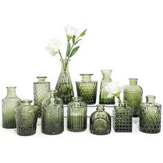 a collection of green glass vases with white flowers in the middle one is empty