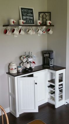 there is a coffee bar with cups on the shelf above it and two mugs hanging from the wall