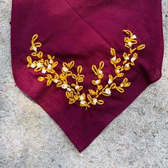 a purple bandana with yellow and white embroidered flowers on the front, sitting on concrete