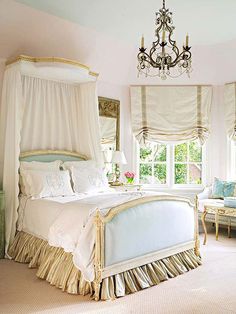 a white bed sitting under a chandelier in a bedroom next to a window