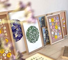 four framed pictures with flowers on them sitting on top of a wooden table next to an open book