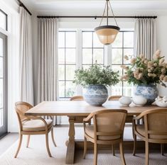 a dining room table with chairs and vases on it's centerpiece in front of a large window