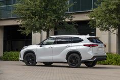 a white toyota highland parked in front of a building with trees and bushes around it