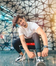 a man sitting on top of a red chair in front of a wall with geometric designs