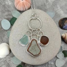 three sea glass pendants sitting on top of a rock next to seashells