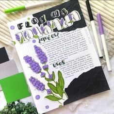 an open book with purple flowers and green leaves next to some writing utensils