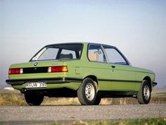 an old green car is parked on the side of the road in front of some grass