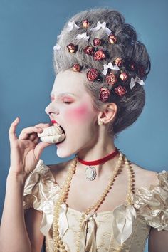 a woman with flowers in her hair is eating a doughnut while wearing pearls and necklaces