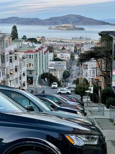 many cars parked on the side of a road next to some buildings and water in the background