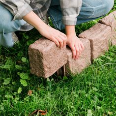 a person kneeling down on top of a brick in the grass with their hands resting on it