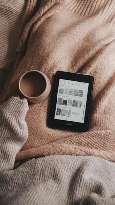 an electronic device sitting on top of a bed next to a cup of coffee