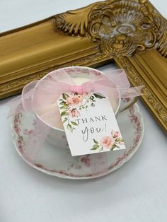 a cup and saucer with a thank you tag on it next to a gold frame