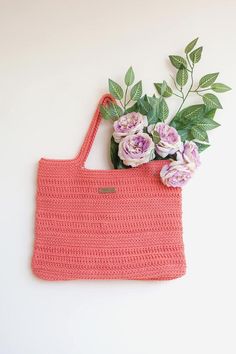 a crocheted bag with flowers in it sitting on a table next to a plant