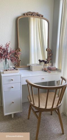 a white desk with a mirror, chair and vase on it in front of a window