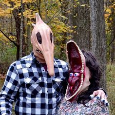 a man and woman wearing masks in the woods with trees behind them, one has a large beak on his head