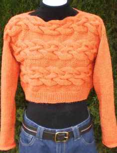 an orange sweater is displayed on a mannequin's head with grass in the background