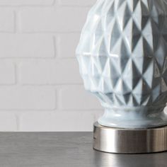 a white vase sitting on top of a metal table next to a brick wall in the background