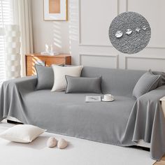 a living room with a gray couch covered in grey sheets and white pillows on the floor