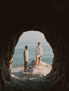 two people are standing in the middle of a cave by the ocean, looking out at the water