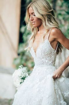 a woman in a white wedding dress holding a bouquet and looking down at her left shoulder