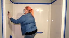 a woman is painting the walls of a bathroom with blue tape and paint rollers