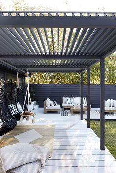 an outdoor living area with black furniture and white rugs on the floor, covered by a pergolated roof