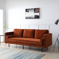 an orange couch sitting on top of a hard wood floor next to a white wall