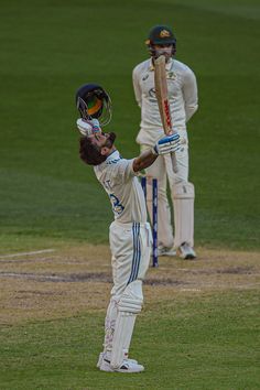 a man holding a baseball bat on top of a field next to another man in white uniform