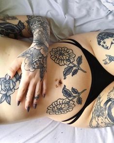 a tattooed woman laying on top of a bed next to a white sheet covered in tattoos