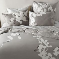 a bed with grey and white flowers on the comforter, pillows and pillow cases