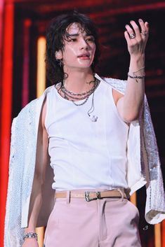 a male in a white shirt and pink pants on stage with his hand up to the air