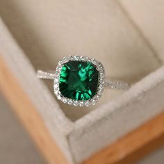 a ring with a green stone surrounded by white diamonds in a box on top of a wooden table